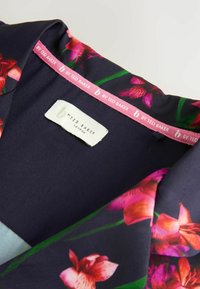 Navy bloes met bloemenpatroon in levendige roze en groene tinten, met een zachte textuur en een label met de tekst "By Ted Baker London."