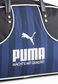 Blå og sorte stribede Puma taske med hvide kanter og sølvnitter, med Puma-logo og teksten "MACHT'S MIT QUALITÄT".