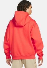 Fleece hoodie, ljus korallfärg, oversize-modell, stor huva, ribbade ärmslut och nederkant, slät textur, inga synliga mönster eller logotyper.