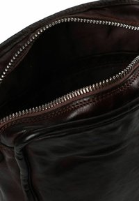 Interno di una borsa in pelle marrone con chiusura a zip, caratterizzato da una texture liscia e da una cerniera metallica.