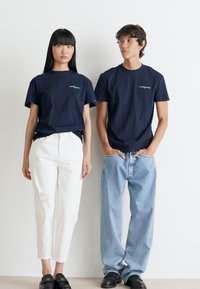 Navy cotton t-shirts with short sleeves and a small logo, paired with white distressed jeans and light blue loose-fit jeans. Black slip-on shoes.