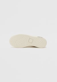 Egy off-white sportcipő talpa, amelyen a felületek tapadásmintázata látható, valamint egy kis négyzet alakú logó a közepén, sima háttérrel.