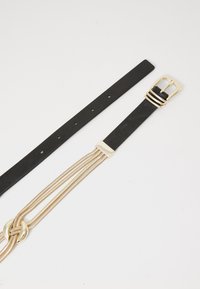 Zwarte faux leren riem met een gouden metalen gesp en meerdere gouden kettingstrengen ter versiering. Platte uitvoering zonder zichtbare patronen.