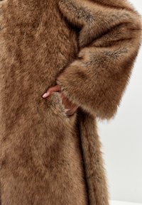 Faux fur frakke i diverse nuancer af brunt; blød, tæt tekstur med brede ærmer og sidelommer.