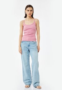 Roze geribbelde tanktop met dunne bandjes, gecombineerd met lichtblauwe wijde jeans. Schoeisel: sandalen met open tenen. Soepele textuur en casual pasvorm.