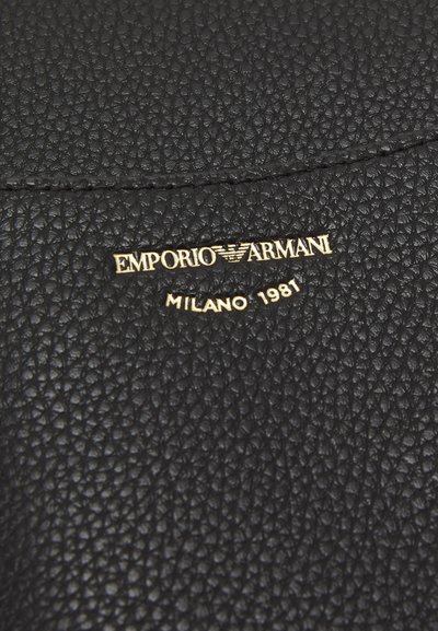 Juodas akmeninis odos paviršius su reljefiniu tekstūru, viduryje esantis auksinis logotipas su užrašu "EMPORIO ARMANI MILANO 1981".