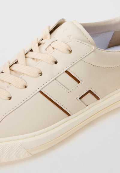 Beige low-top leather sneaker with cream laces, perforated "H" logo on side, and textured rubber sole.