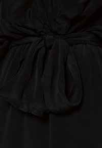 Gros plan d'une ceinture en tissu noir nouée avec de doux plis et une texture, serrant un vêtement noir à la taille.
