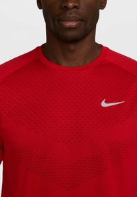 Crvena Nike kratka sportska majica s kratkim rukavima koja se odlikuje teksturiranim uzorkom na tkanini, okruglim izrezom i malim sivim logotipom na prsima.
