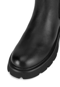 Czarny skórzany botek za kostkę z zaokrąglonym noskiem, teksturowaną powierzchnią i grubą, wytrzymałą gumową podeszwą z głębokim bieżnikiem. Bez widocznych ozdób.