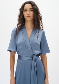 Hellblaues Wickelkleid aus strukturiertem Stoff, mit tiefem V-Ausschnitt, kurzen Ärmeln und einem gebundenen Gürtel in der Taille.