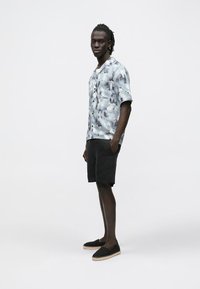 Camisa de manga corta con botones en azul claro con un patrón de acuarela, combinada con pantalones cortos negros y alpargatas negras con detalles de cuerda.