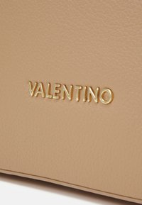 Lys beige lær med en pebbled tekstur, hvor "VALENTINO" er preget med gullbokstaver, noe som fremhever merkevaren.