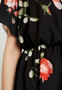Vestido negro con estampados florales en tonos rojos y blancos, con cintura fruncida y textura suave y fluida. Mangas cortas visibles.