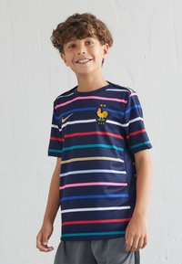 Camiseta de Nike de color azul marino con rayas horizontales en rosa, rojo, verde, amarillo y azul. Presenta un emblema de gallo y la inscripción FFF.
