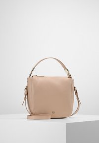 Beige kožená kabelka s texturovaným povrchem, s jedním horním držadlem, odnímatelným ramenním popruhem a malým kovovým logem na přední straně, vystavená na bílém podstavci.