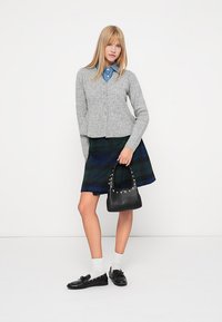 Γκρι ριχτό καζάκι, επικαλυμμένο με μπλε πουκάμισο με γιακά, συνδυασμένο με καρό φούστα σε σκούρο πράσινο και μπλε. Μαύρη τσάντα ώμου με καρφίτσες.