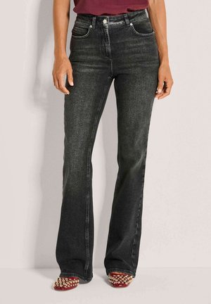 Zwarte flare jeans met hoge taille, gecombineerd met een kastanjebruine top en rode puntige schoenen versierd met gouden studs.