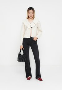 Kremsfarget strikket cardigan med stor krage, sorte tettsittende jeans, røde loafers og en liten svart håndveske med tvinnede håndtak.