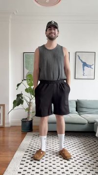 Grå randig linne och svarta shorts, matchat med vita strumpor och bruna tofflor. Står på en mönstrad matta med en växt i närheten.