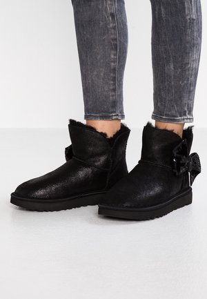 Bottines noires à la cheville avec doublure duveteuse et détail nœud en sequins, portées avec un jean skinny gris délavé.
