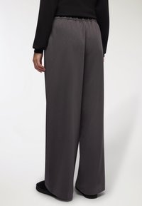 Pantaloni a gamba larga in tessuto grigio scuro, con una cintura elastica e una texture liscia e leggera. Nessun motivo o accento visibile.