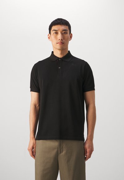 Sort polo shirt med korte ærmer, flad krave og to-knaps lukning. Båret med khaki bukser, minimalistisk design, glat tekstur.