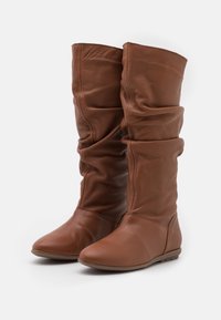 Bottes en cuir marron décontractées montantes jusqu'aux genoux, à bouts ronds et semelles plates, présentant une texture lisse et des détails minimes.