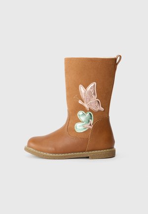 Botte enfant couleur sable avec des appliqués de papillons roses et verts sur le côté, semelle plate et languette à l’arrière, présentée sur un fond uni.