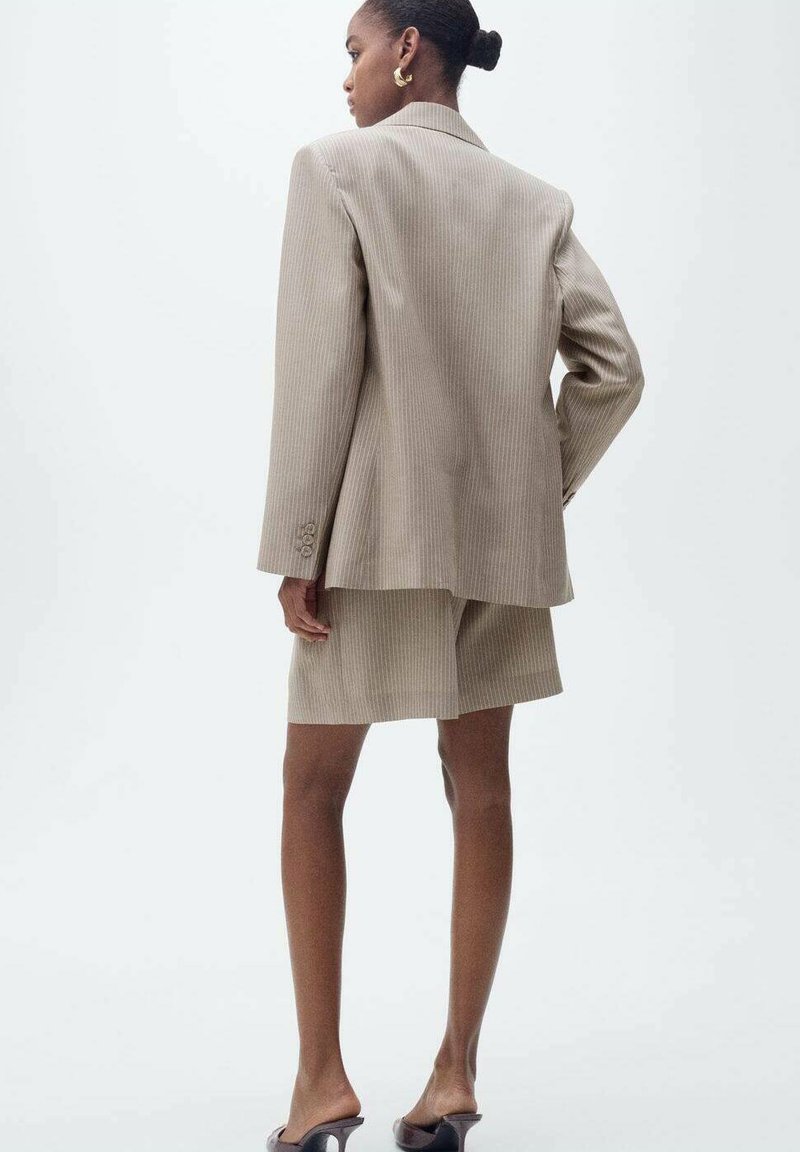 Blazer beige a righe sottili con pantaloni coordinati, caratterizzato da una vestibilità su misura e una texture liscia. Accentuato da un solo bottone e un design elegante.