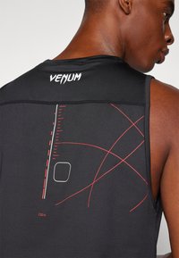 Top sportivo senza maniche di colore nero con tessuto a rete. Presenta linee grafiche rosse a contrasto e il nome del marchio "VENUM" sul collo posteriore.
