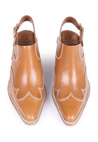 Scarpe in pelle marrone con punta affusolata, design a scallop ritagliato e una piccola cinghia alla caviglia con fibbia dorata. Cuciture dettagliate visibili.