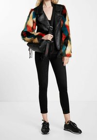Czarna skórzana kurtka z rękawami z wielobarwnego sztucznego futra; w połączeniu z czarnymi obcisłymi jeansami i czarnymi trampkami z wzorzystymi akcentami.