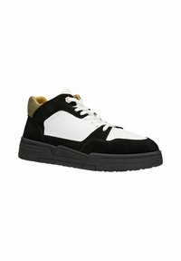 Zwart-witte sneaker van suède en rubber, met een geperforeerde neus, gewatteerde kraag en contrasterende groene accenten op de hak.
