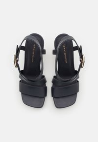 Mustikka nahkaiset korkokengät, joissa on kaksi leveää remmiä jalkapöydän ympäri, kapea nilkkaremmi ja neliön muotoinen kärki. Kulttoneiset solkit.