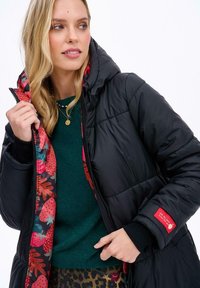 Čierna prešívaná bunda s kvetinovou podšívkou, na ktorej sú červené jahody. Obsahuje kapucňu a rebrované manžety, so znakom nezameniteľnej nášivky.