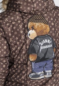 Giubbotto imbottito marrone con motivo logo su tutta la superficie. Orsetto ricamato sul retro, che indossa una maglietta nera con "GIANNI KAVANAGH."