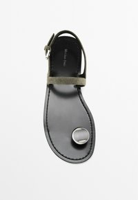Sandalo in suede verde oliva con due cinturini e un'accensione circolare in argento su una suola in pelle nera. Presenta una cinghia alla caviglia regolabile.