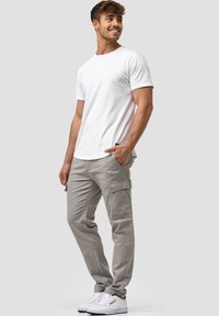 Weißes Baumwoll-T-Shirt mit Rundhalsausschnitt, kombiniert mit hellgrauen Cargo-Hosen mit Seitentaschen und schmalem Schnitt, ergänzt durch weiße Sneaker.