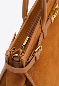 Brązowa torebka ze zamszu i skóry z złotymi elementami, z zamknięciem na zamek błyskawiczny i podwójnymi uchwytami. Gładka tekstura i wyraźny kształt.