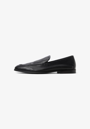 Mocassins en cuir noir avec une texture lisse, bout légèrement pointu, accents repliés sur le dessus et une semelle en caoutchouc à profil bas.