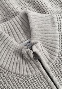 Hellgrauer Strickpullover mit hohem Kragen, ribbelstruktur und einem halben Reißverschluss am Hals; Etikett innen sichtbar.