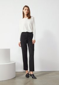 Top blanco de manga larga con un corte relajado, combinado con pantalones ajustados negros y tacones negros de punta. Diseño minimalista, textura suave.