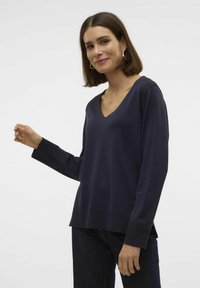 Pull en V en laine marine à manches longues, avec des bords côtelés et une coupe décontractée. Le tissu a une texture lisse, avec des fentes sur les côtés à l'ourlet.