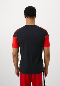 Kortærmet sportstrøje i sort stof med røde detaljer og gule sidelister, rund hals og afslappet pasform.