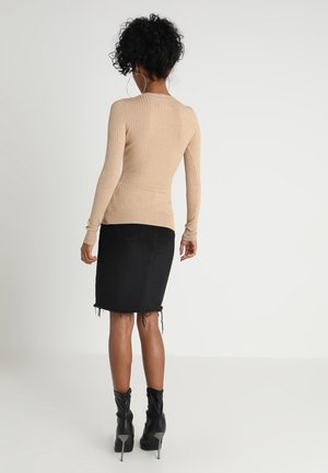 Maglietta a maniche lunghe beige a costine abbinata a una gonna di jeans nera con orlo sfrangiato. Il modello indossa stivali con tacco neri e grandi orecchini a cerchio.