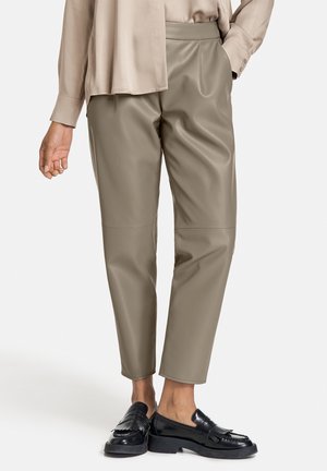 Pantaloni in finta pelle beige chiaro con gamba affusolata, caratterizzati da un'alta vita e da una texture liscia, abbinati a mocassini neri.