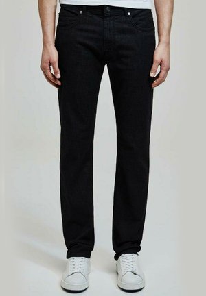 Jean en denim noir avec une coupe droite. Comprend des poches avant, des coutures discrètes et une fermeture à bouton. Porté avec des sneakers blanches.