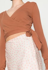Camisola castanha de mangas longas, com transpassado à frente e decote em V, combinada com uma saia branca com padrão floral em rosa e verde.