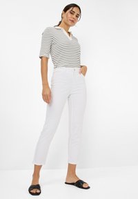 Haut à manches courtes rayé avec décolleté en V ; associé à un jean droit blanc et des sandales noires à enfiler. Matière en coton lisse, coupe décontractée.